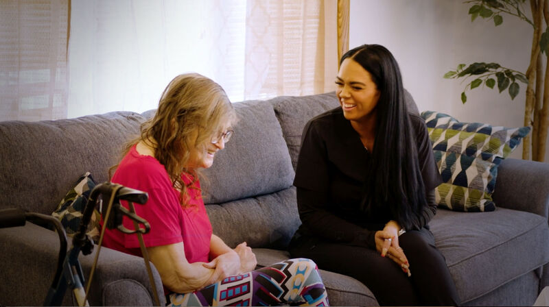 A caregiver sitting and talking with a woman on a living-room sofa