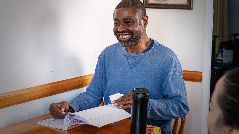 A smiling man working through an activity book at the kitchen table