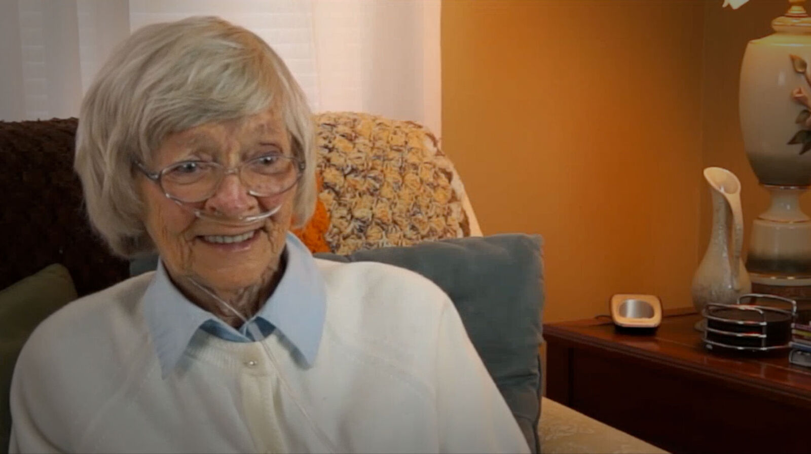 An older woman smiling in her armchair at home